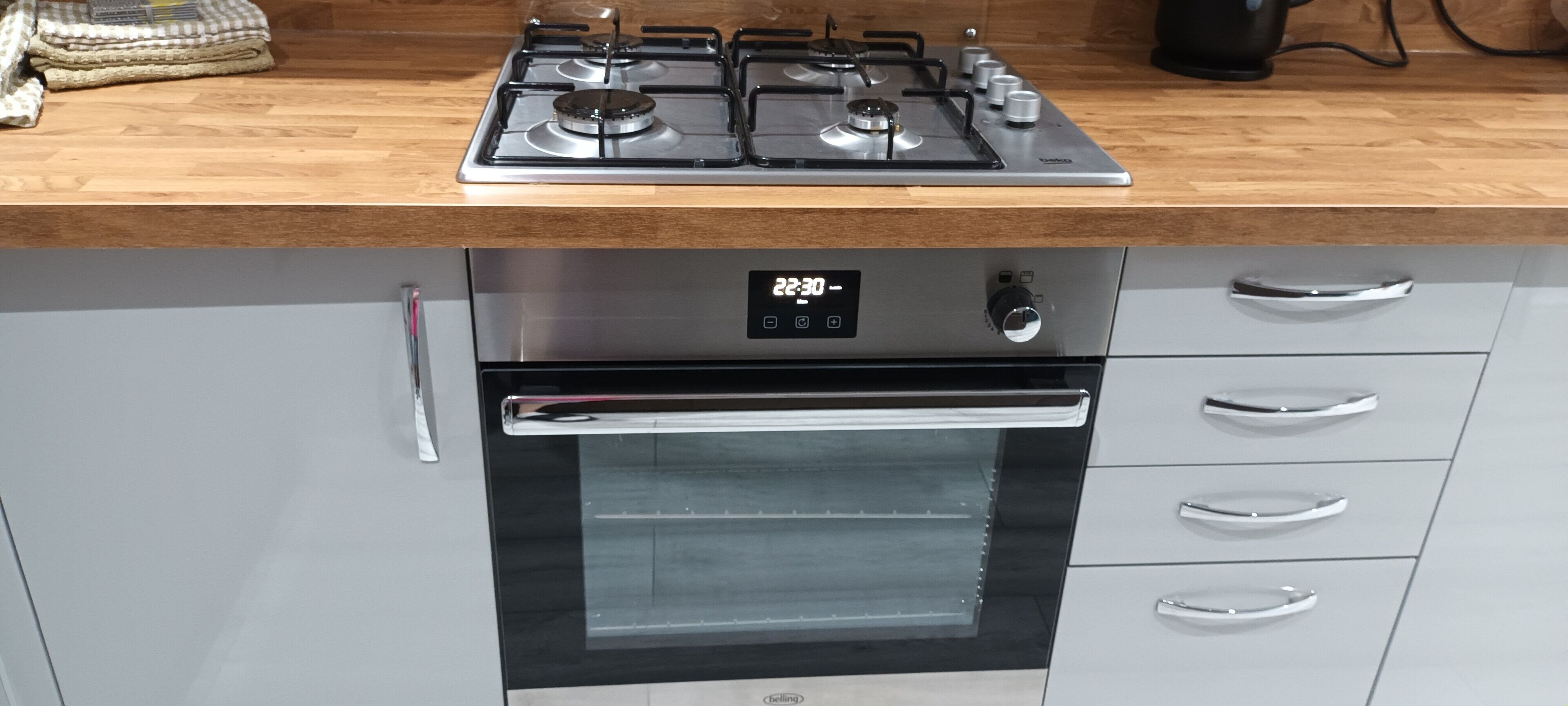 A kitchen with a stainless steel gas stove, oven, and a digital clock displaying 22:30.