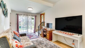 Una sala de estar con un sofá, un televisor, un escritorio y una escalera que lleva a un área exterior.