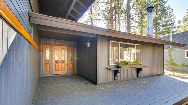 Une terrasse en bois avec un bâtiment gris doté d’une grande fenêtre et d’une porte.