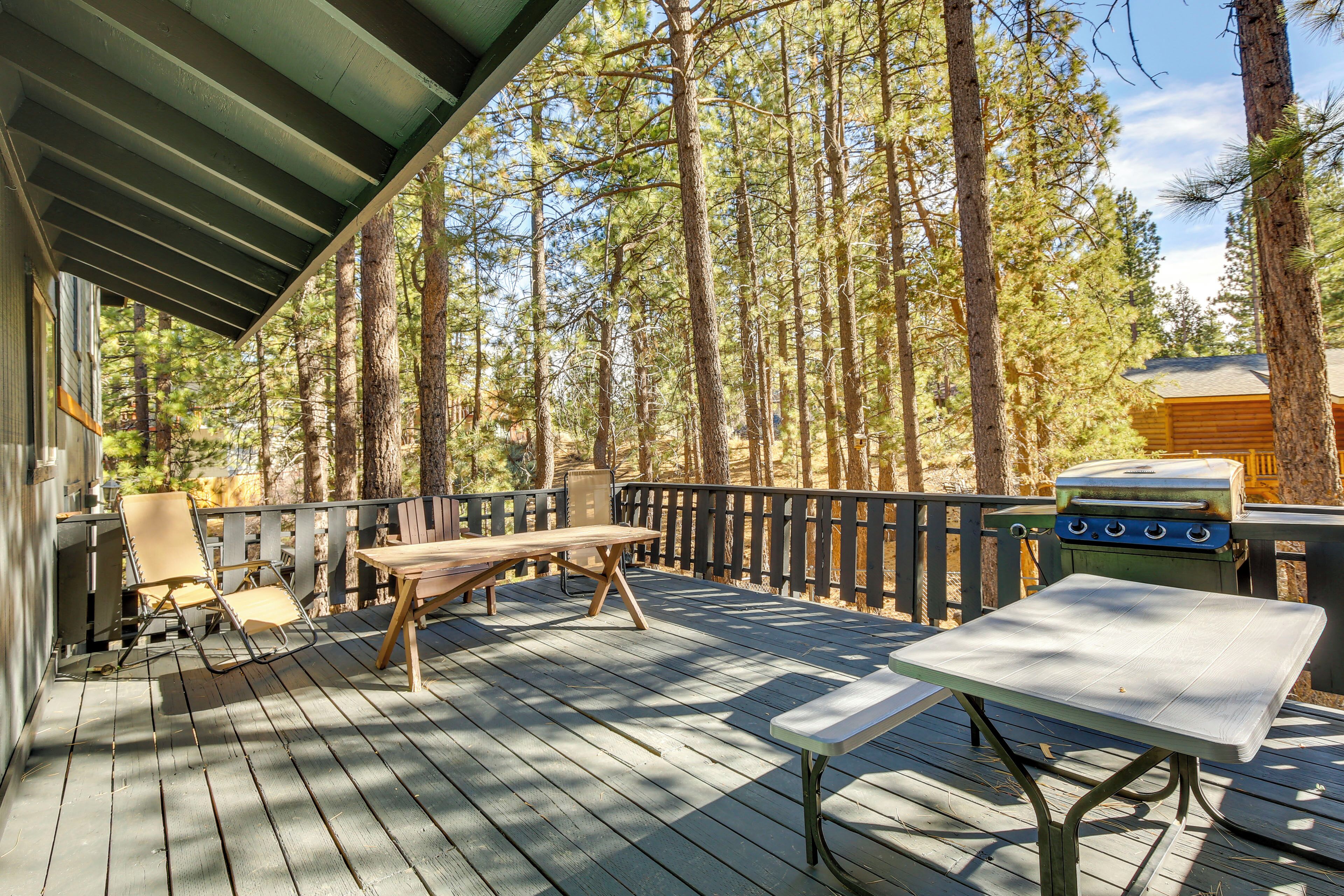 A wooden deck with a table and chairs, surrounded by tall trees.