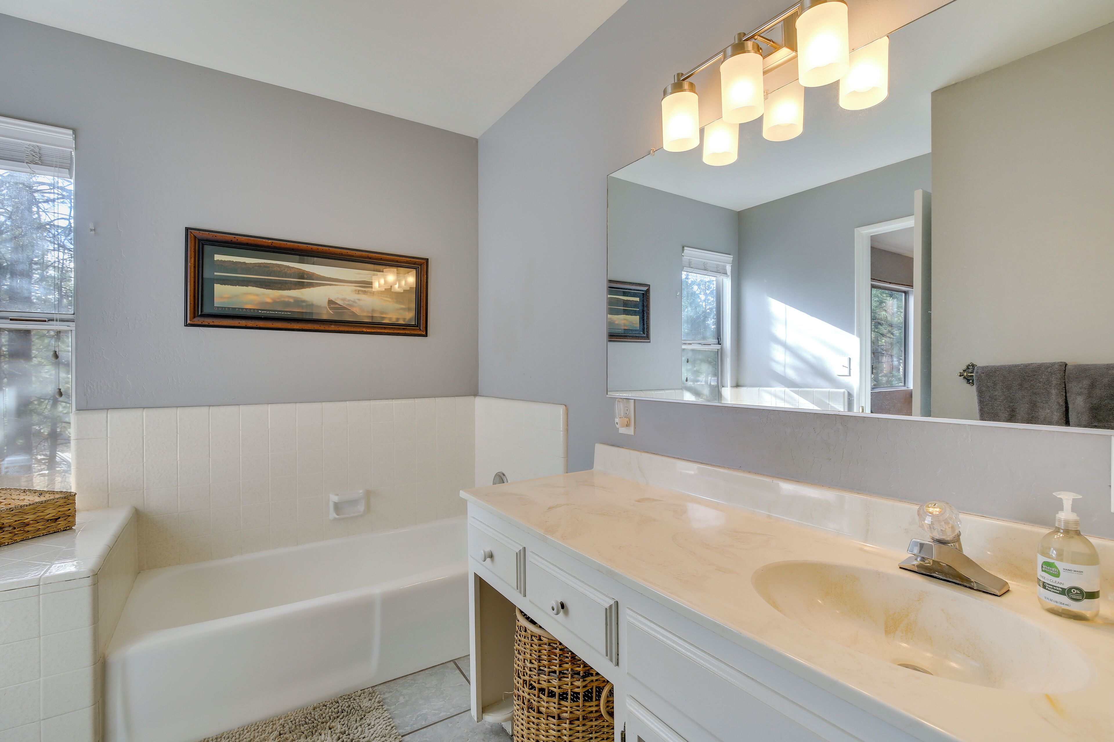 A modern bathroom with a bathtub, a large mirror, and a sink with a soap dispenser.
