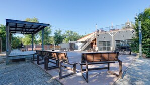 An outdoor patio with wooden benches and a covered seating area, surrounded by a gravel path and a fence. - The Merlot Bungalow Defiance Tiny Home on Trail (Defiance)
