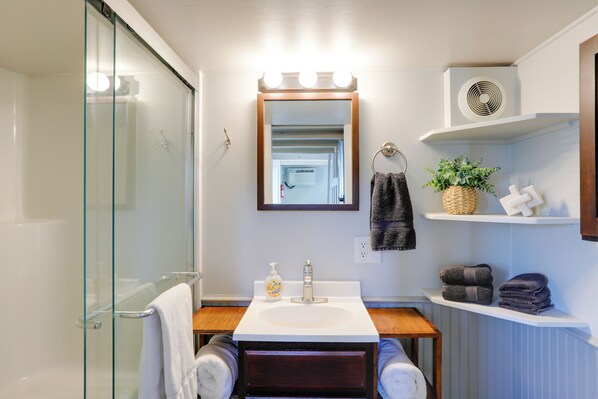 A bathroom with a glass shower enclosure, a sink with a mirror above it, and a towel rack. - The Merlot Bungalow Defiance Tiny Home on Trail (Defiance)