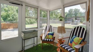 A sunroom with large windows, a wooden chair with colorful cushions, a small table, and a birdhouse decoration. - 'the Cabernet Cabin' Defiance Home on Katy Trail! (Defiance)