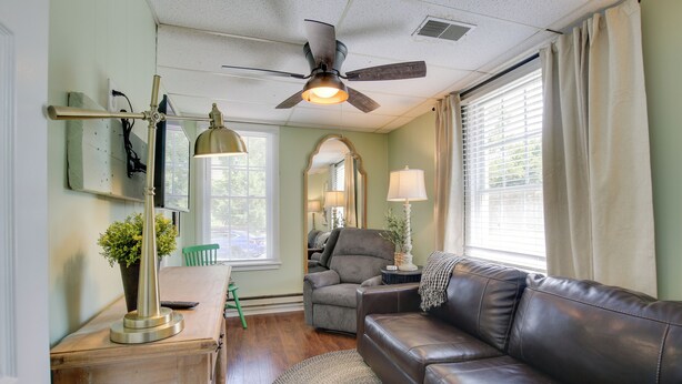 A cozy living room with a leather couch, a wooden table, a ceiling fan, and a large window with curtains. - 'the Cabernet Cabin' Defiance Home on Katy Trail! (Defiance)