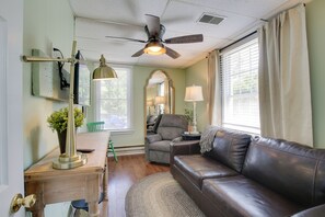 A cozy living room with a leather couch, a wooden table, a ceiling fan, and a large window with curtains. - 'the Cabernet Cabin' Defiance Home on Katy Trail! (Defiance)
