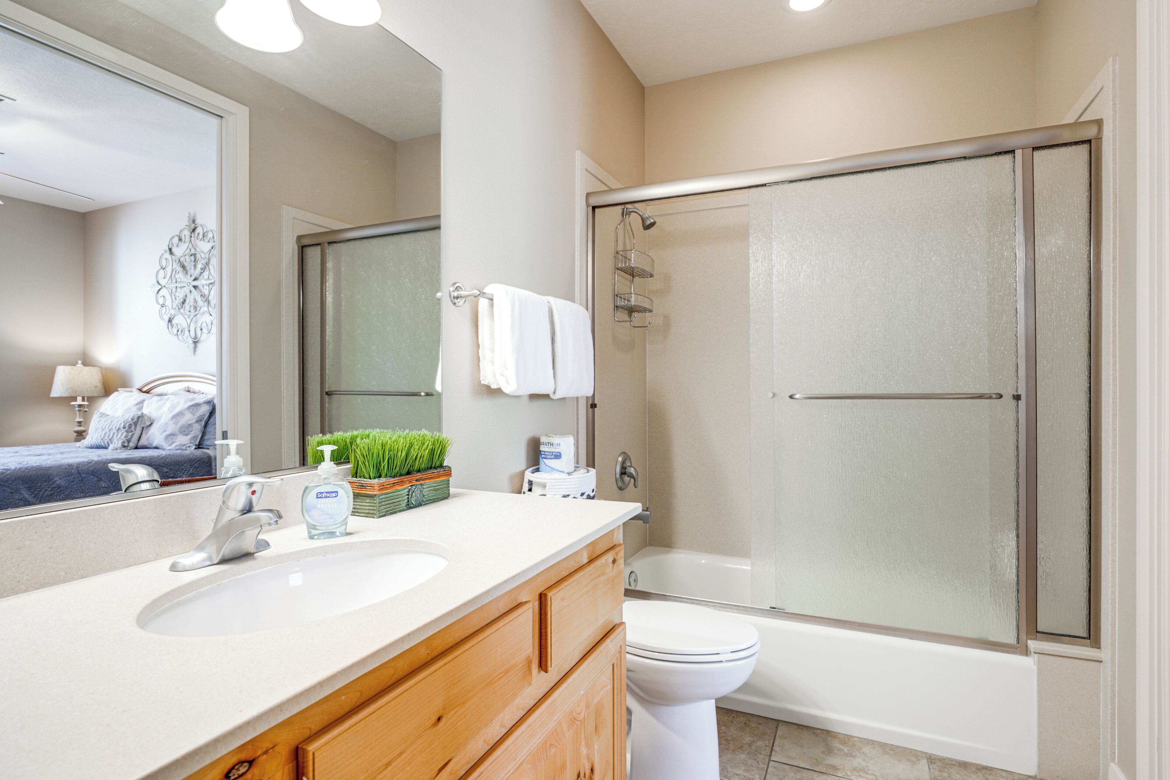 A modern bathroom with a large mirror, a white sink, a toilet, and a glass-enclosed shower.