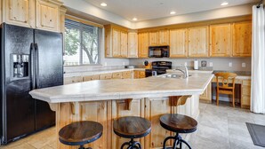 A modern kitchen with wooden cabinets, a large island with stools, a black refrigerator, and a microwave. - Pool Access & Patio! Resort-style St George Condo (St. George)