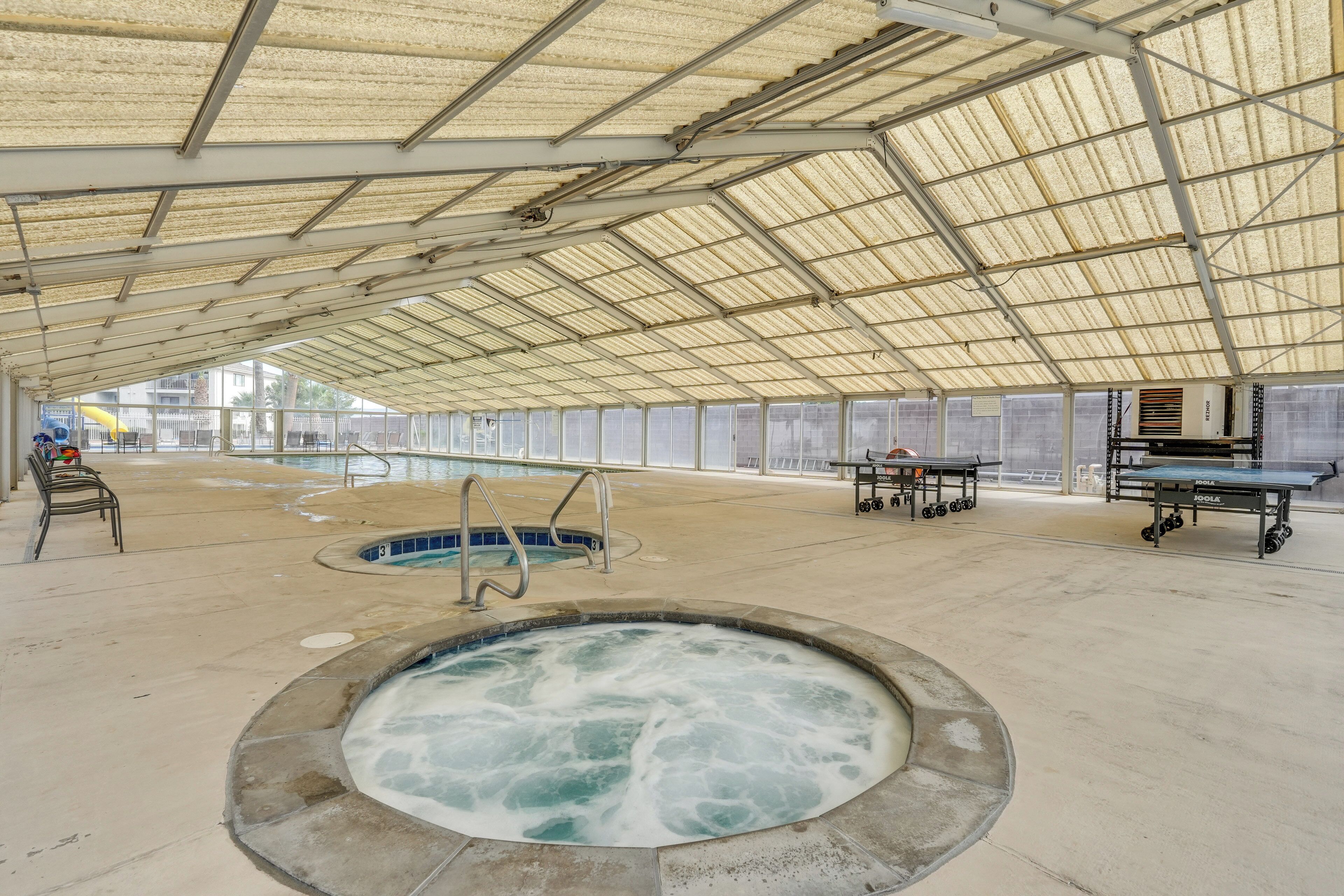 An indoor swimming pool area with a hot tub, exercise equipment, and a covered roof structure.