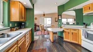 A kitchen with wooden cabinets, a white countertop, and a dining area with chairs and a table. - Lakefront Chiloquin Home w/ Scenic Deck! (Chiloquin)