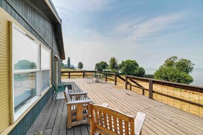 Eine Holzterrasse mit einer Bank und einem Tisch, mit Blick auf ein Gewässer und Bäume.