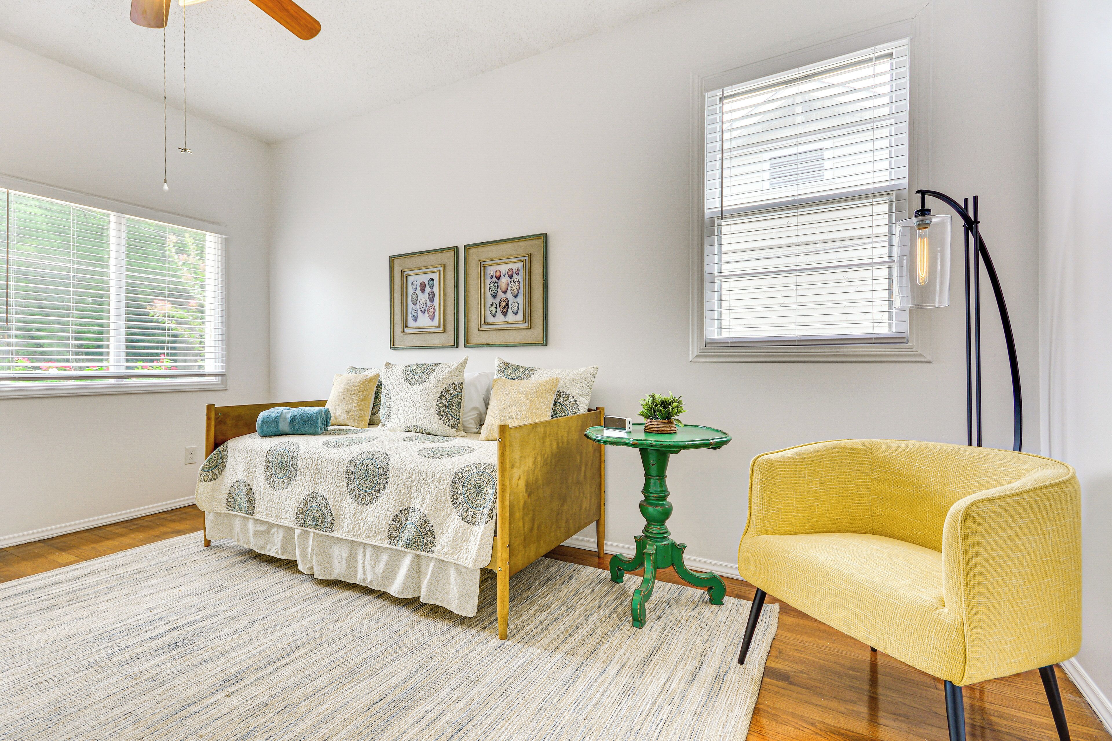 Une chambre à coucher avec un lit, une table verte, un fauteuil jaune et deux tableaux encadrés accrochés au mur.