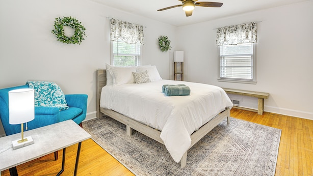 A bedroom with a bed, a blue chair, a bedside table, a floor lamp, and a ceiling fan. - 'dogwood Cottage' w/ Fireplace: 1 Mi to University (High Point)