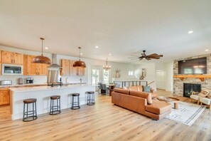 A spacious living area with a large sofa, a fireplace, and a kitchen with wooden cabinets and a central island. - 2 Mi to Lake: Stunning Twin Lakes Home w/ Deck (Twin Lakes)