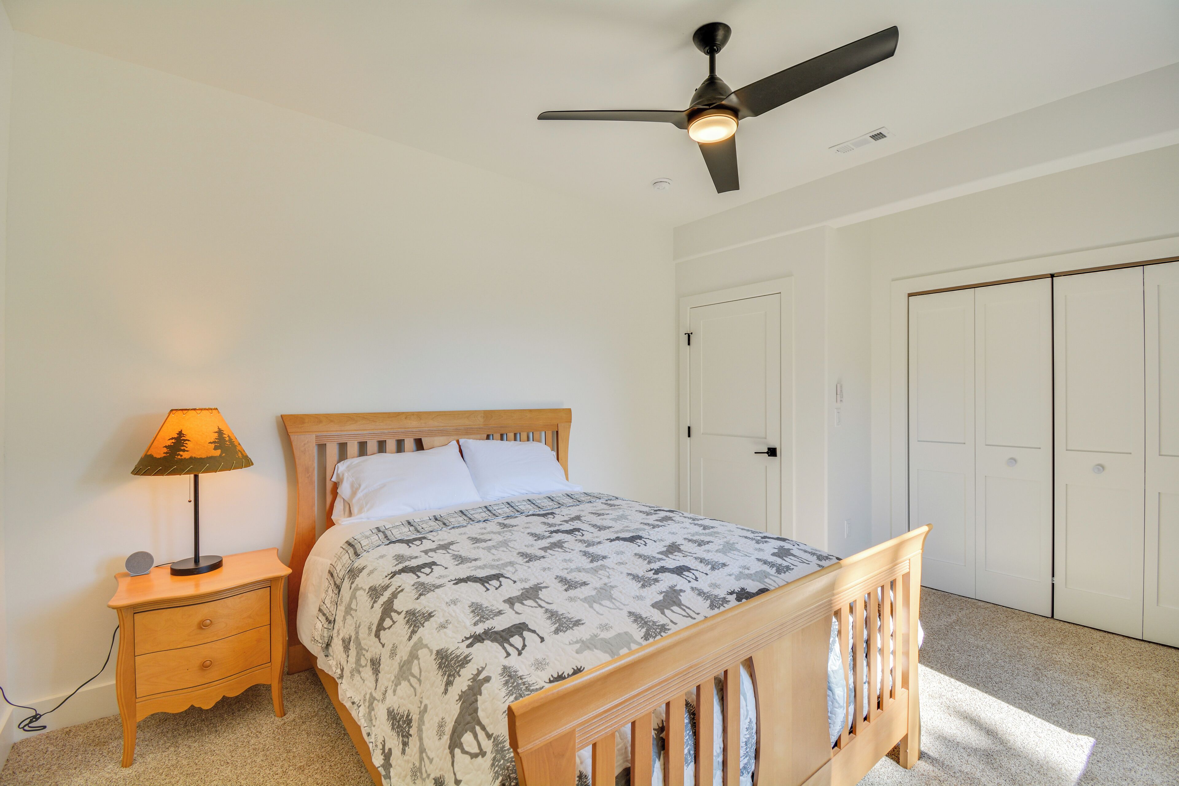 A bedroom with a bed, nightstand, lamp, ceiling fan, and wardrobe.