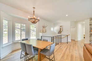 A spacious dining area with a wooden table and grey chairs, a chandelier, and large windows offering a view of the outdoors. - 2 Mi to Lake: Stunning Twin Lakes Home w/ Deck (Twin Lakes)