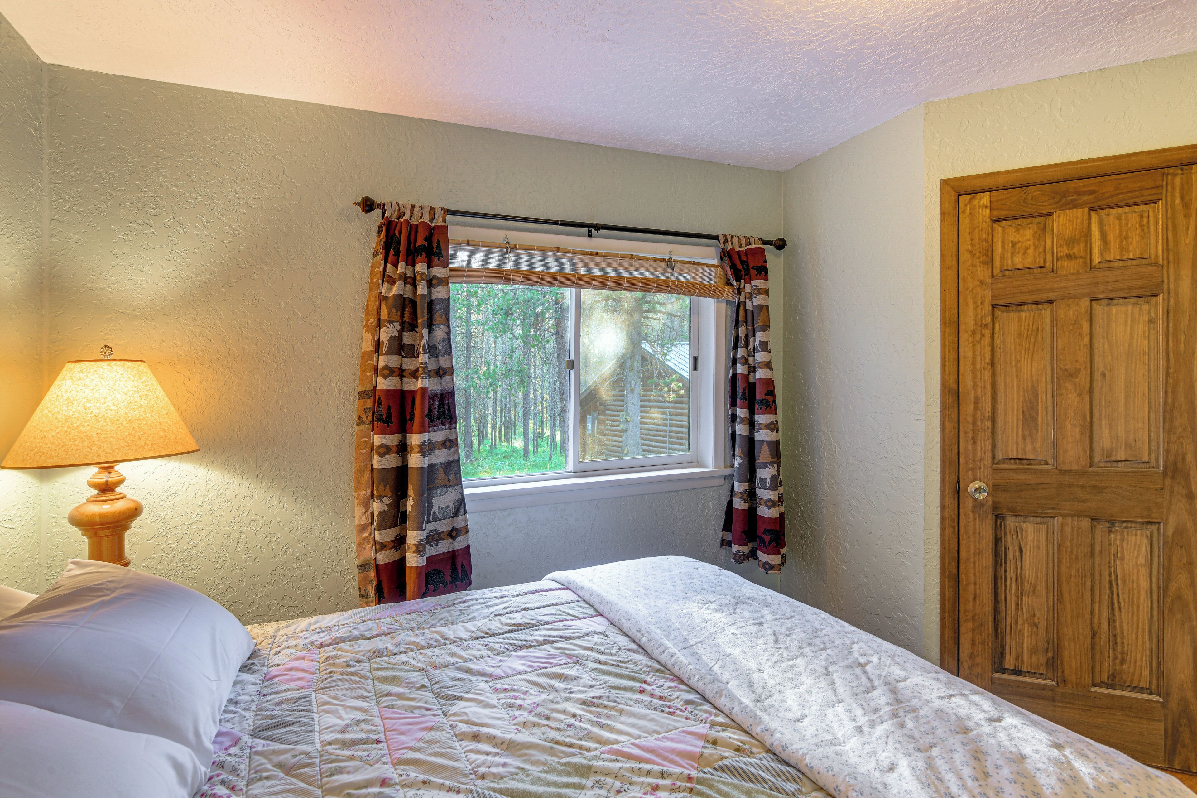 A bedroom with a bed, a window with curtains, a wooden door, and a lamp on a bedside table.