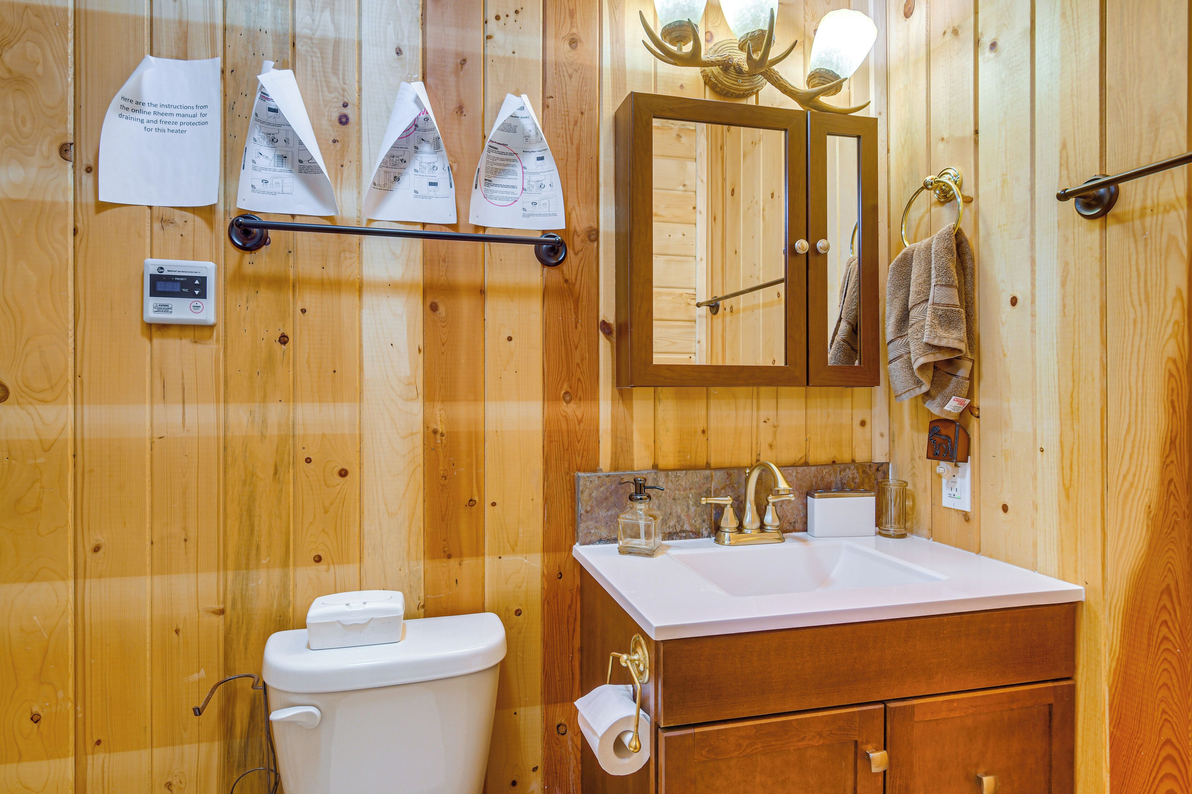 A wooden-paneled bathroom with a toilet, sink, and mirror. Instructions for the heater are visible on the wall.