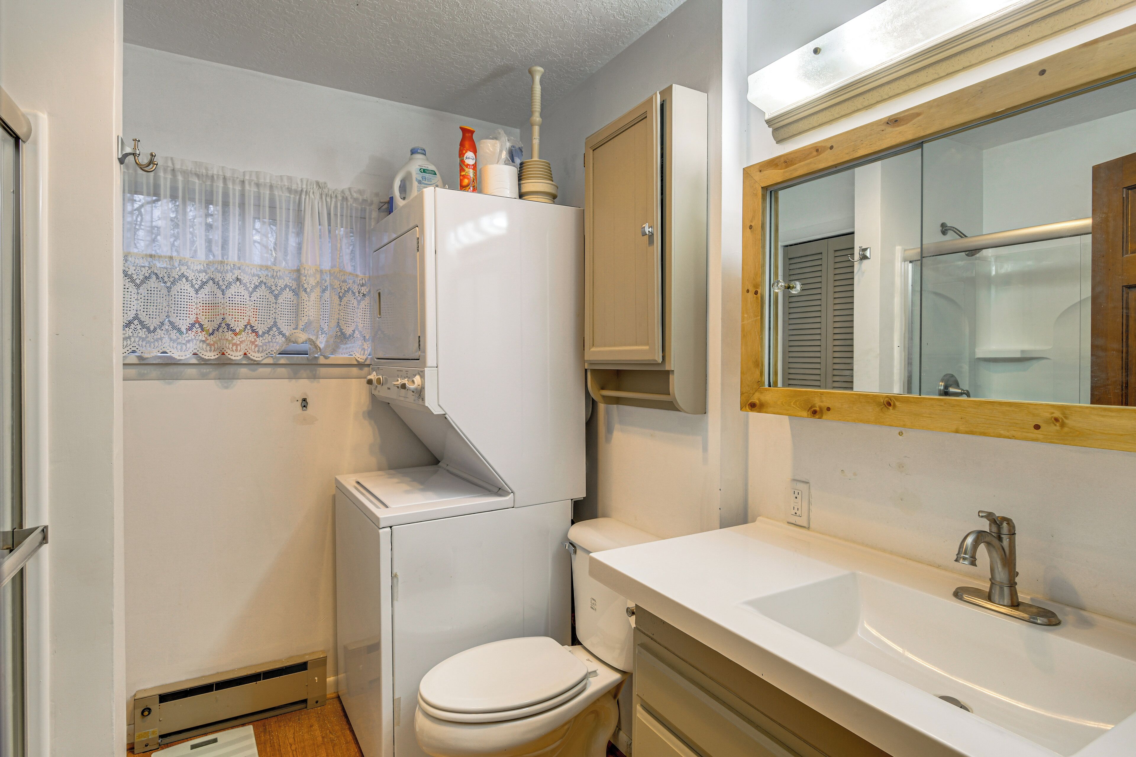 A compact bathroom with a toilet, sink, and a window with lace curtains.