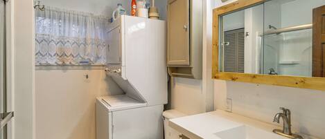 A compact bathroom with a toilet, sink, and a window with lace curtains.