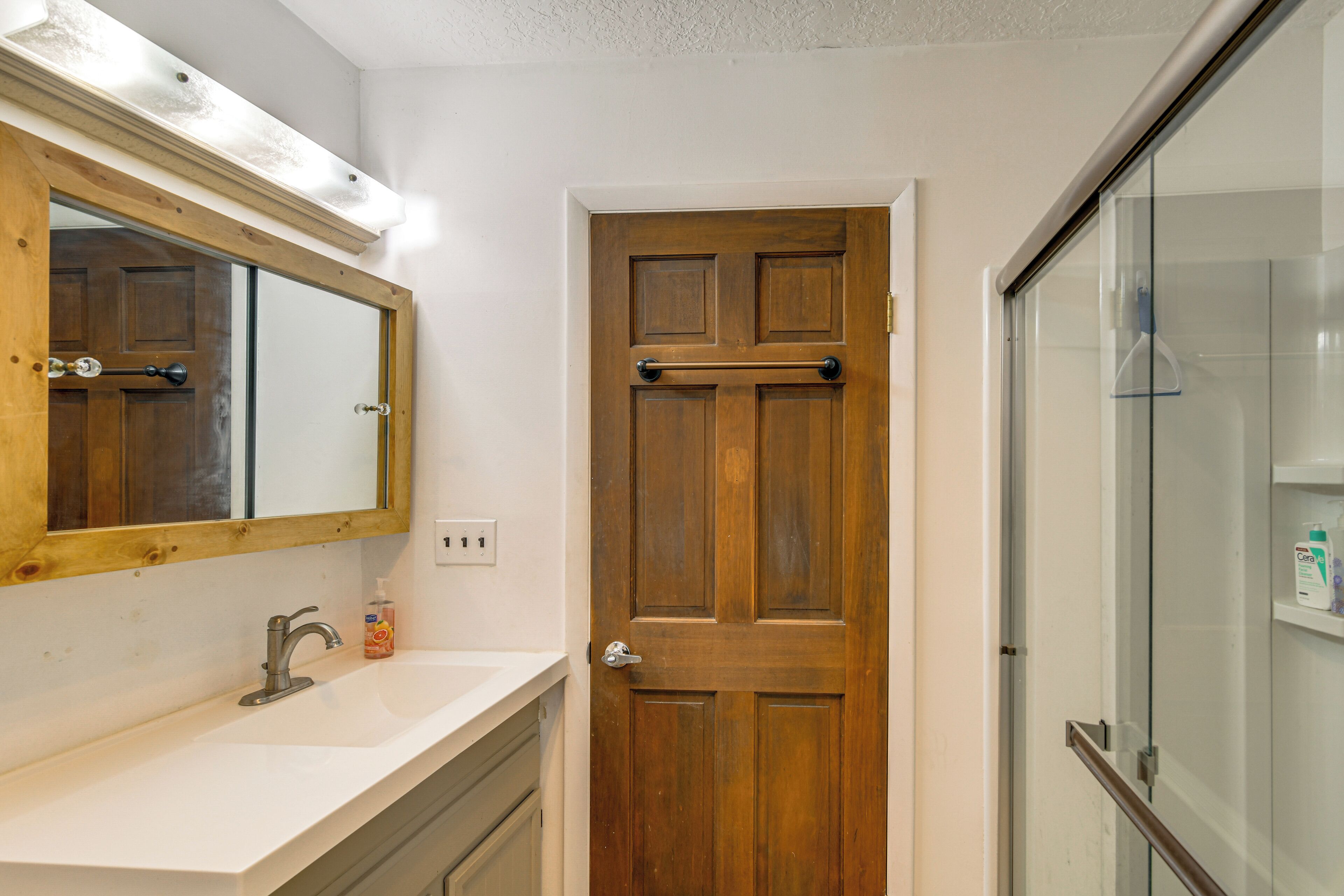 Un baño con puerta de madera, lavamanos blanco y cabina de ducha de vidrio.