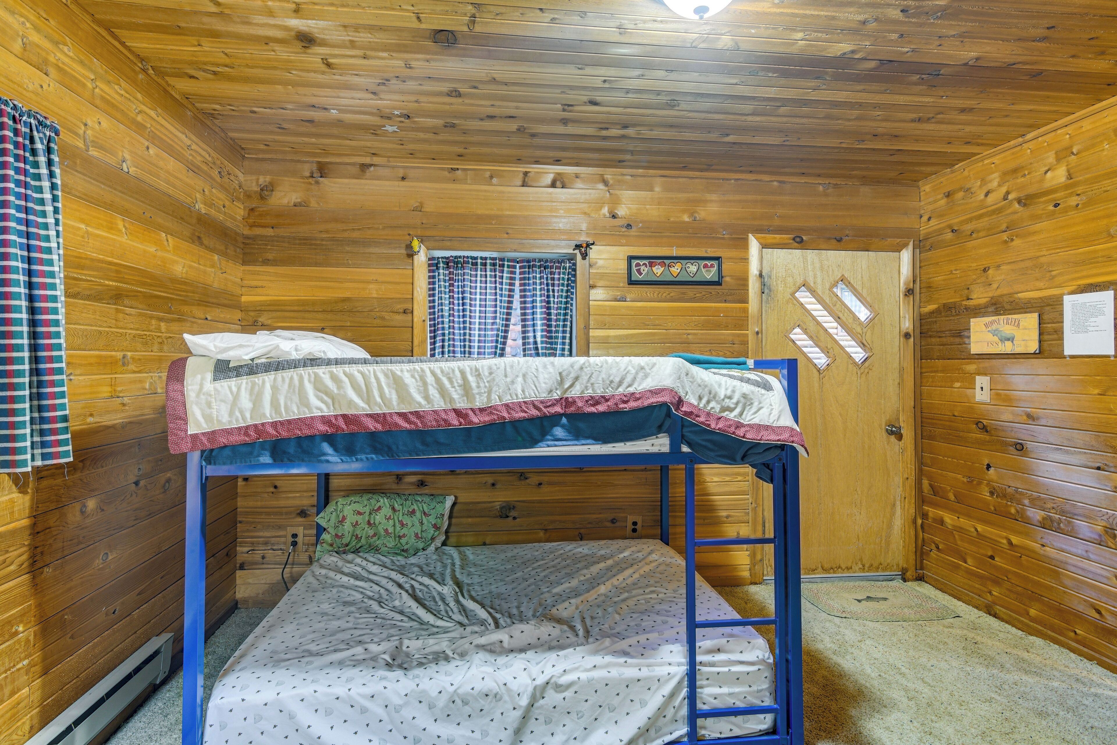 Une chambre avec des lits superposés, des murs en bois, une fenêtre avec des rideaux et une porte décorée d’un motif en forme de cœur.