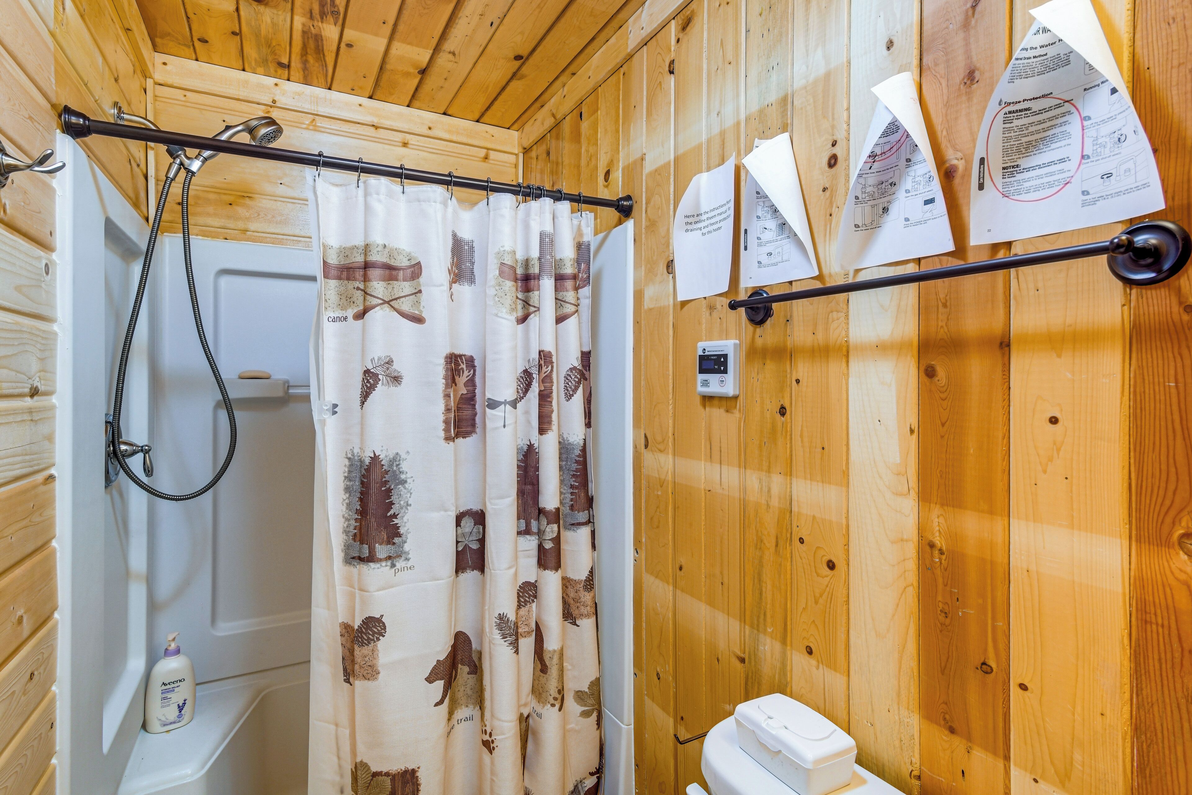 A wooden cabin bathroom with a shower, toilet, and a towel rack with papers.
