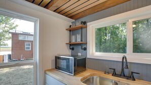 A kitchen with a built-in microwave, stainless steel sink, wooden shelves, and a window overlooking a backyard. - 'the Chardonnay Chalet' Defiance Studio Trail! (Defiance)