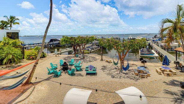 A beachside patio with outdoor seating, palm trees, and a view of the marina. - Key Largo Condo - Community Pool, Marina & Beach! (Key Largo)