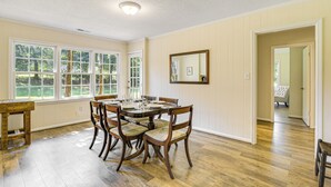 Comedor con mesa y sillas de madera, ventanas amplias y un espejo en la pared.
