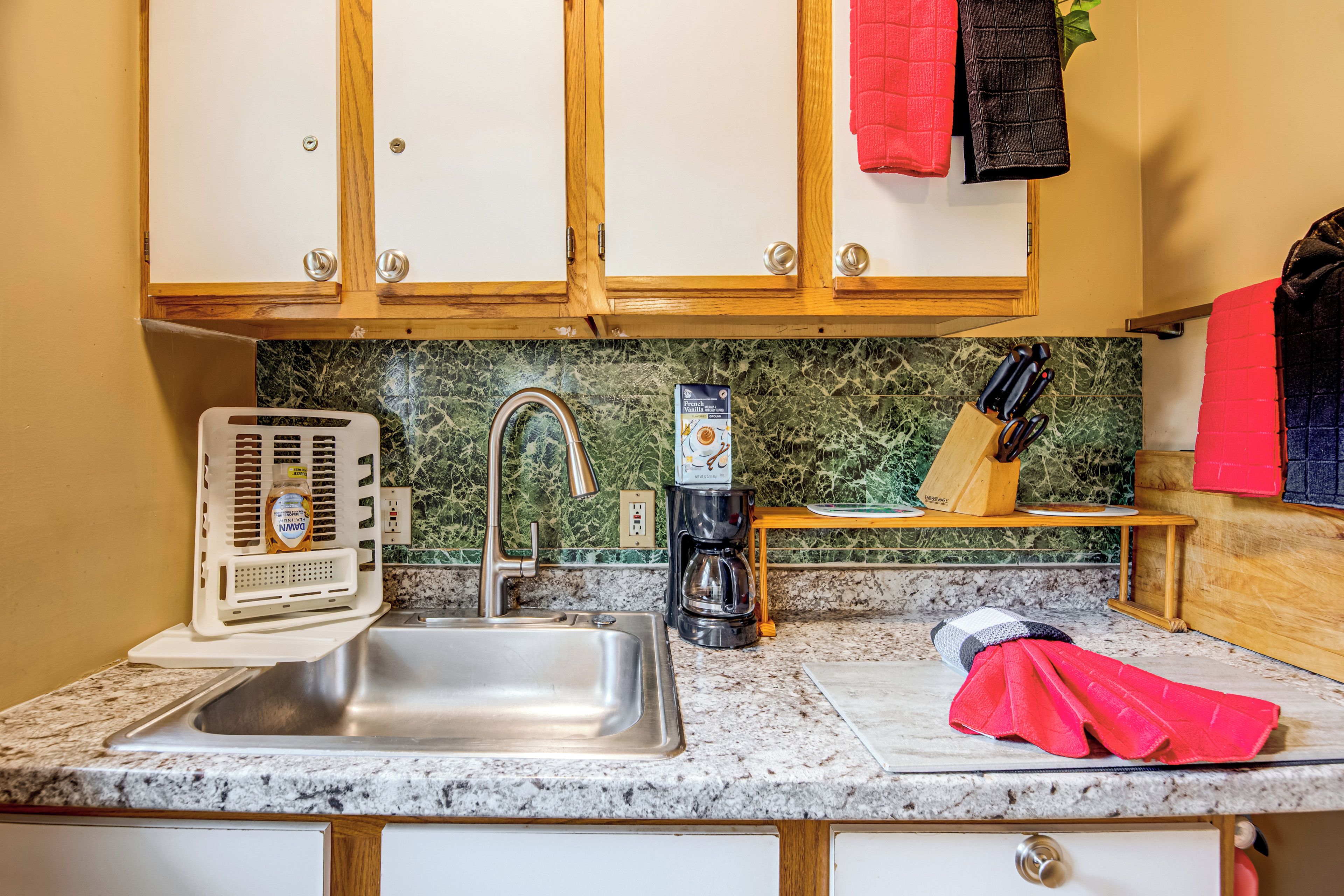 A kitchen with a stainless steel sink, a coffee maker, and a bottle of dish soap.