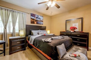 Un dormitorio con cama, mesitas de noche, cómoda, ventilador de techo y un cuadro de la Torre Eiffel.