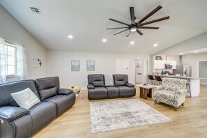 A spacious living area with a ceiling fan, a sofa, a recliner, a patterned armchair, and a kitchen in the background. - Walk to Lake, Parks & Dining: Eufala Family Home! (Eufaula)