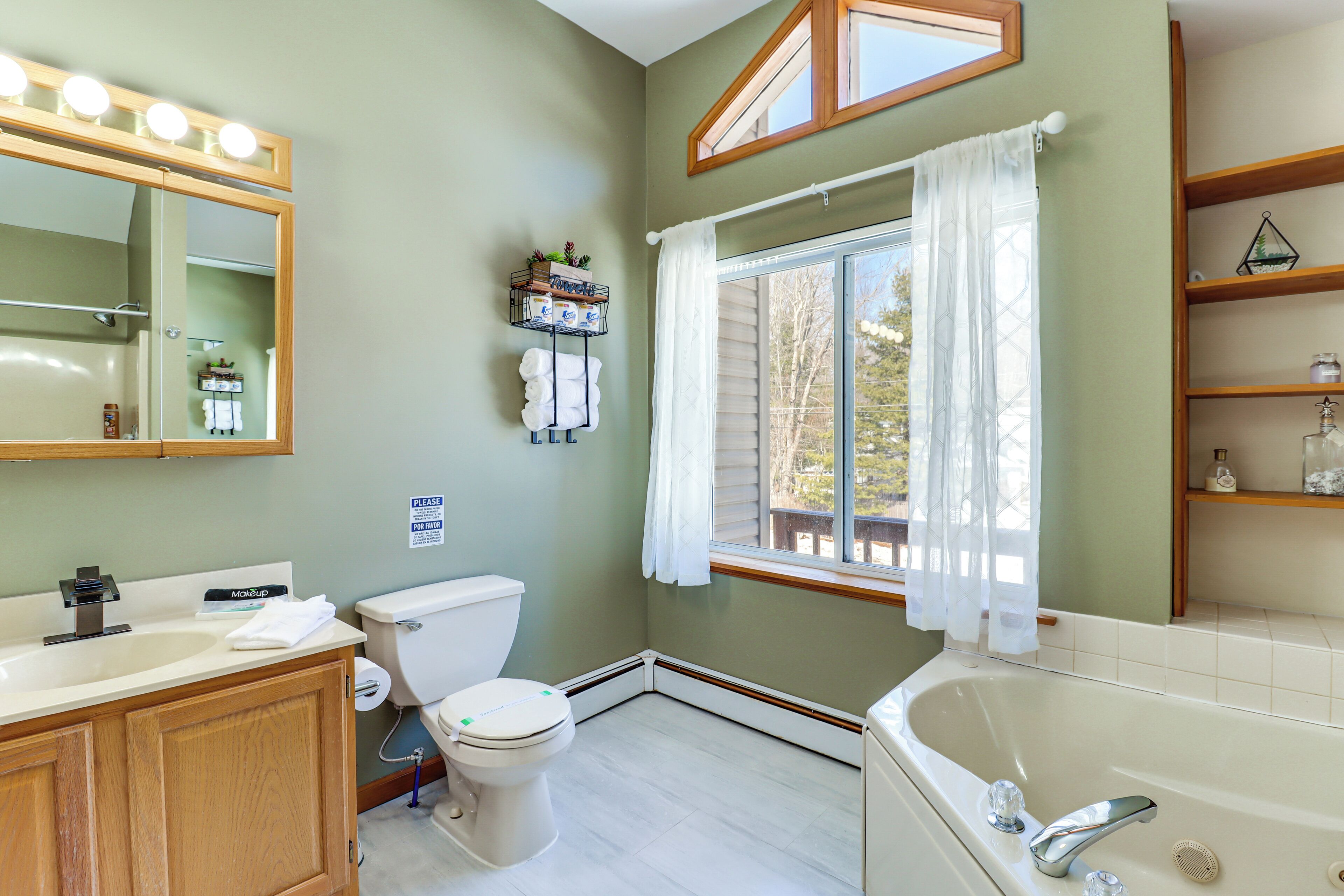 A bathroom with a vanity, toilet, bathtub, and a window with curtains.