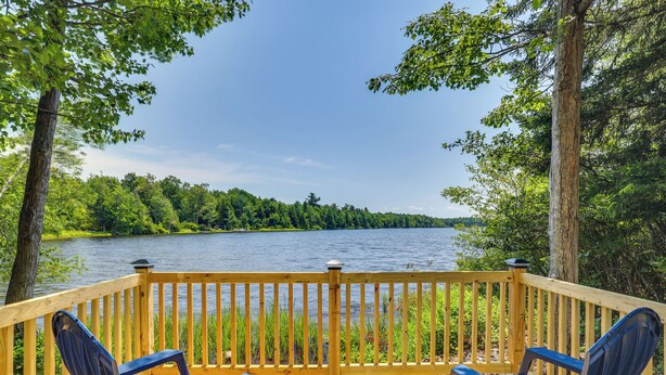 A wooden deck with two blue chairs overlooking a lake surrounded by trees. - Private Hot Tub: Lakefront Poconos Home! (Pocono Summit)