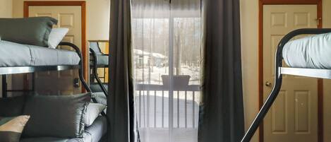 A room with bunk beds, a sofa, and a sliding glass door leading to a balcony.