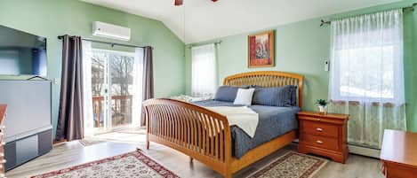 A bedroom with a wooden bed, a ceiling fan, a TV, and a sliding glass door leading to a balcony.