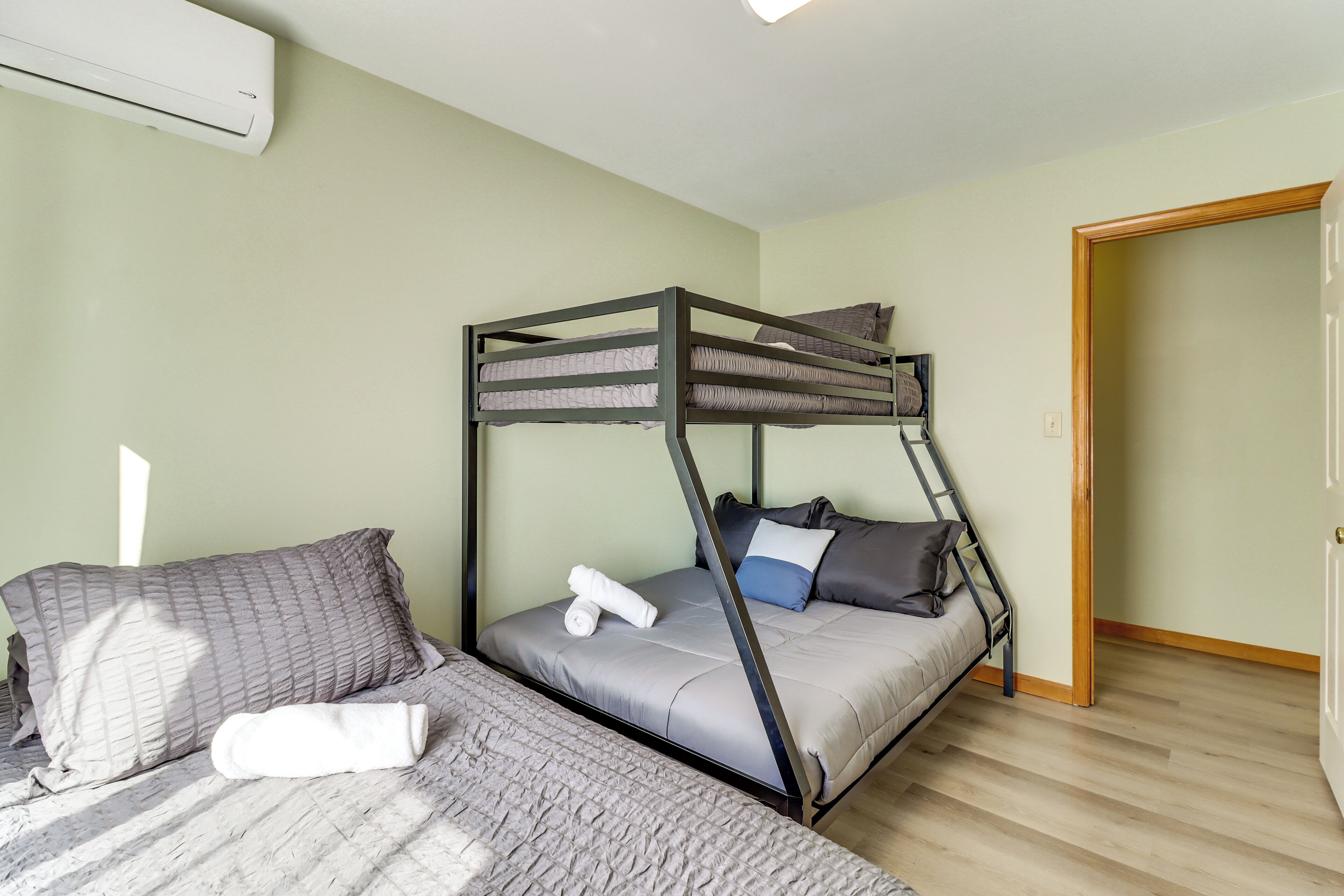 Un lit superposé avec un matelas et des oreillers, une table de chevet et un climatiseur fixé au mur.