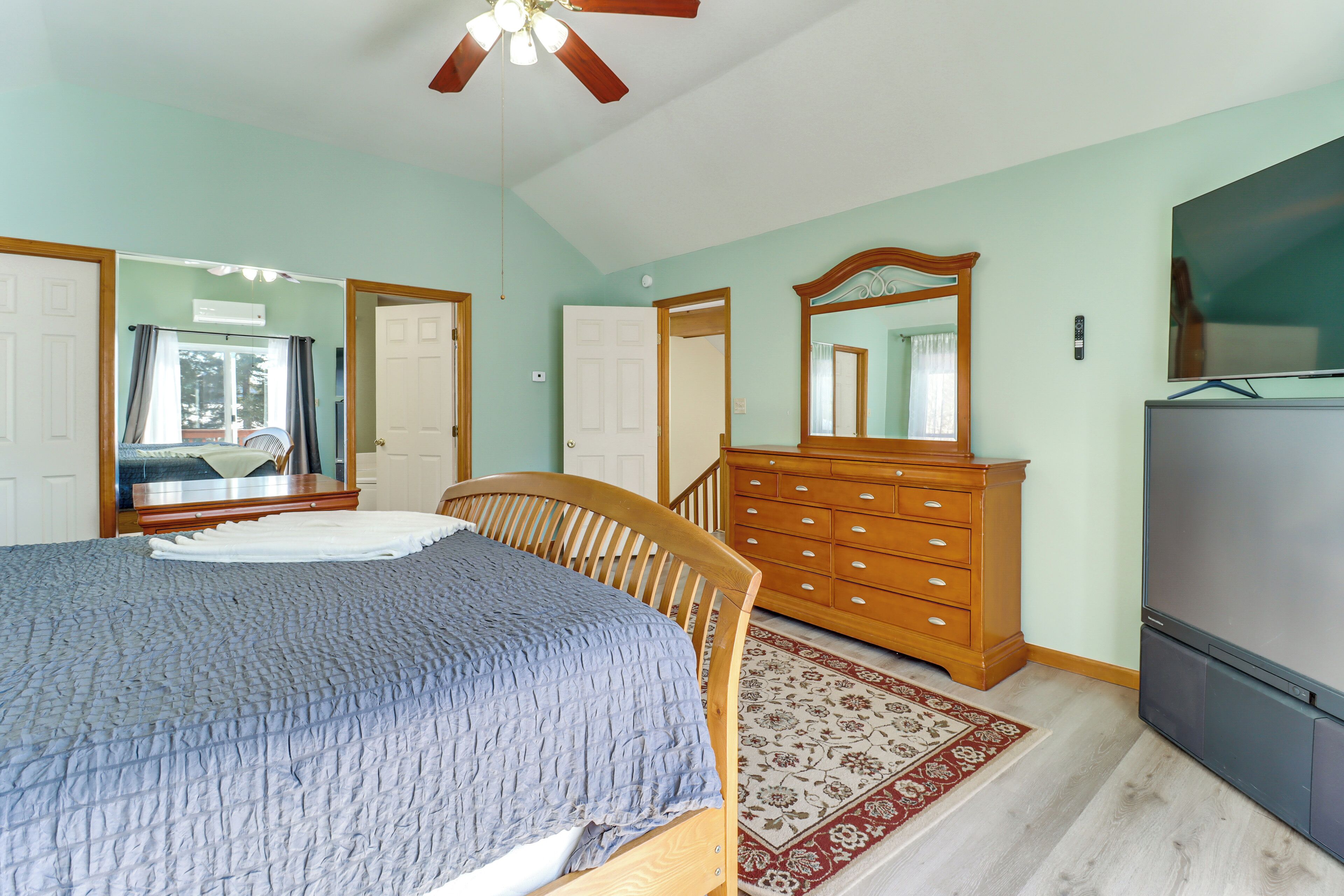 A bedroom with a bed, dresser, mirror, ceiling fan, and TV.