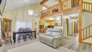 A spacious living room with a dining area, a sofa, and a staircase leading to an upper level. - Private Hot Tub: Lakefront Poconos Home! (Pocono Summit)