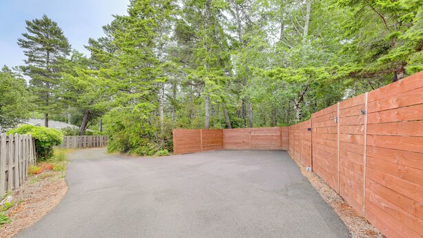 A paved driveway leading to a wooden gate, surrounded by dense greenery and tall trees. - Family-friendly Florence Home: 3 Mi to the Coast! (Florence)