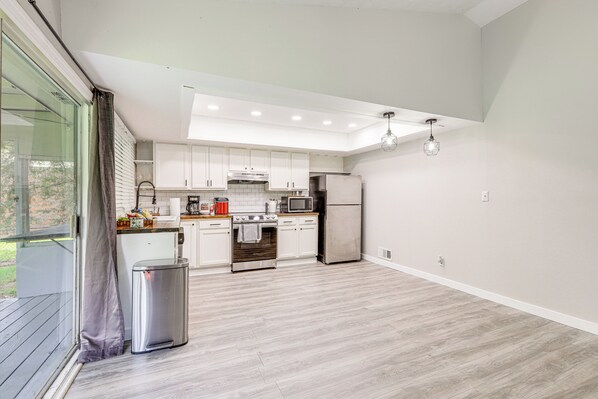 A modern kitchen with white cabinets, stainless steel appliances, and a wooden floor.
