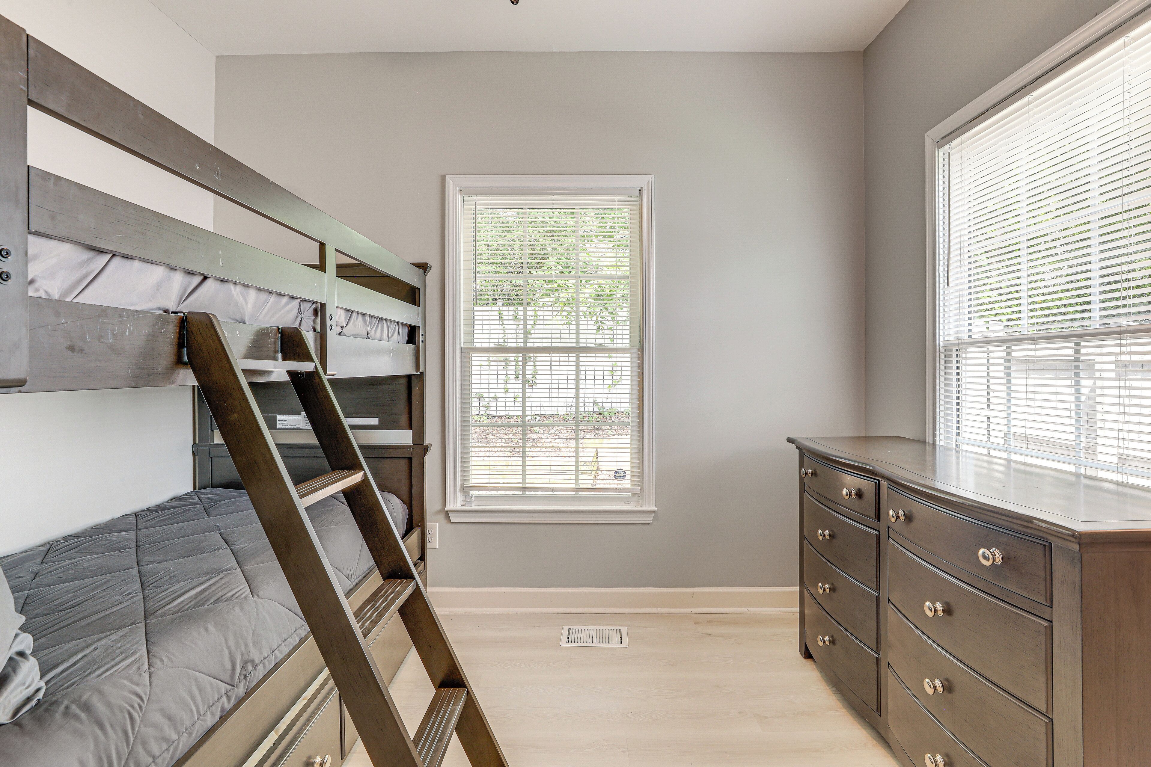 A bedroom with a bunk bed, a dresser, and a window with blinds.