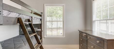 A bedroom with a bunk bed, a dresser, and a window with blinds.