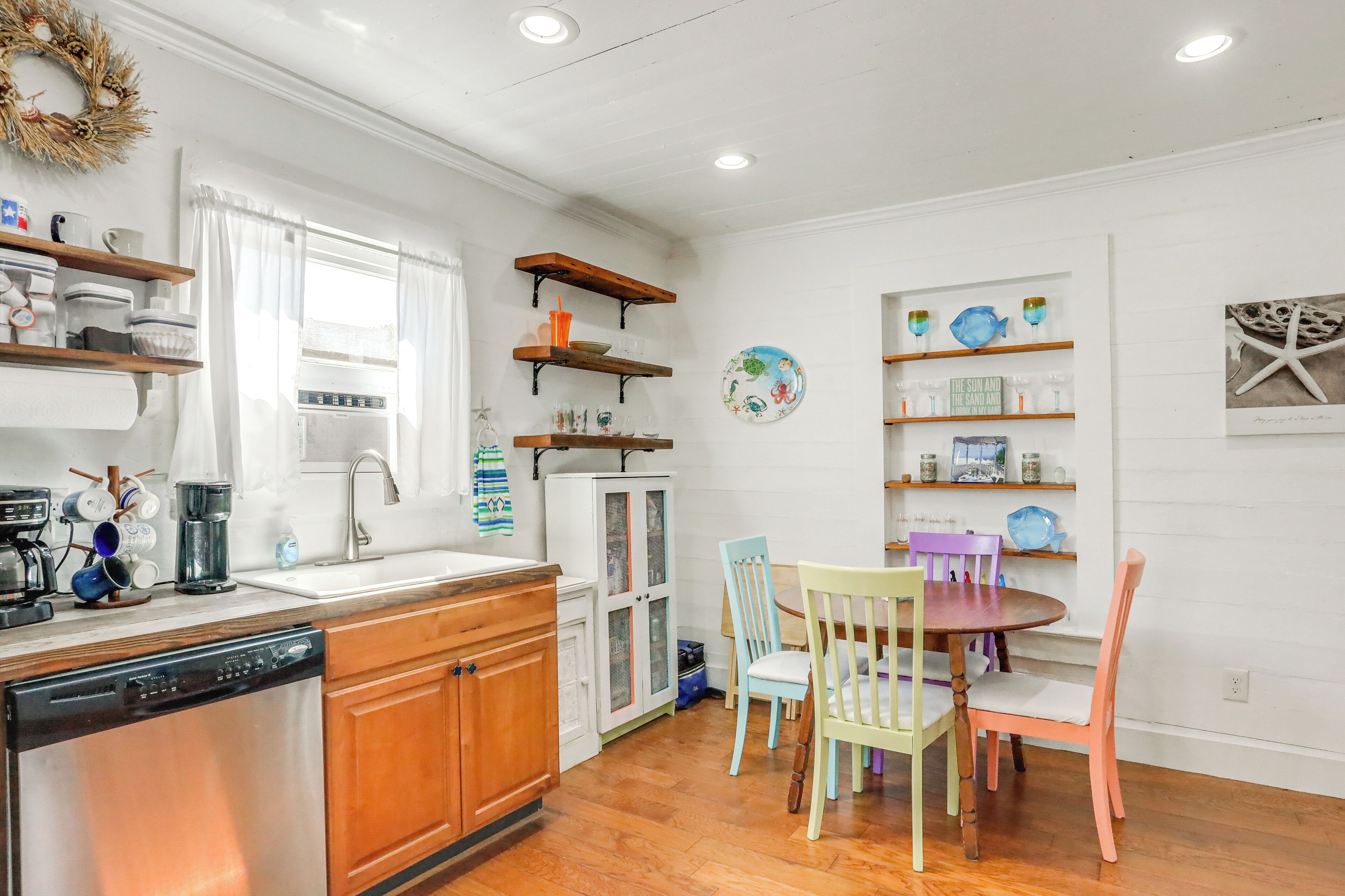 A kitchen with wooden cabinets, a dishwasher, and a dining area with a round table and colorful chairs.