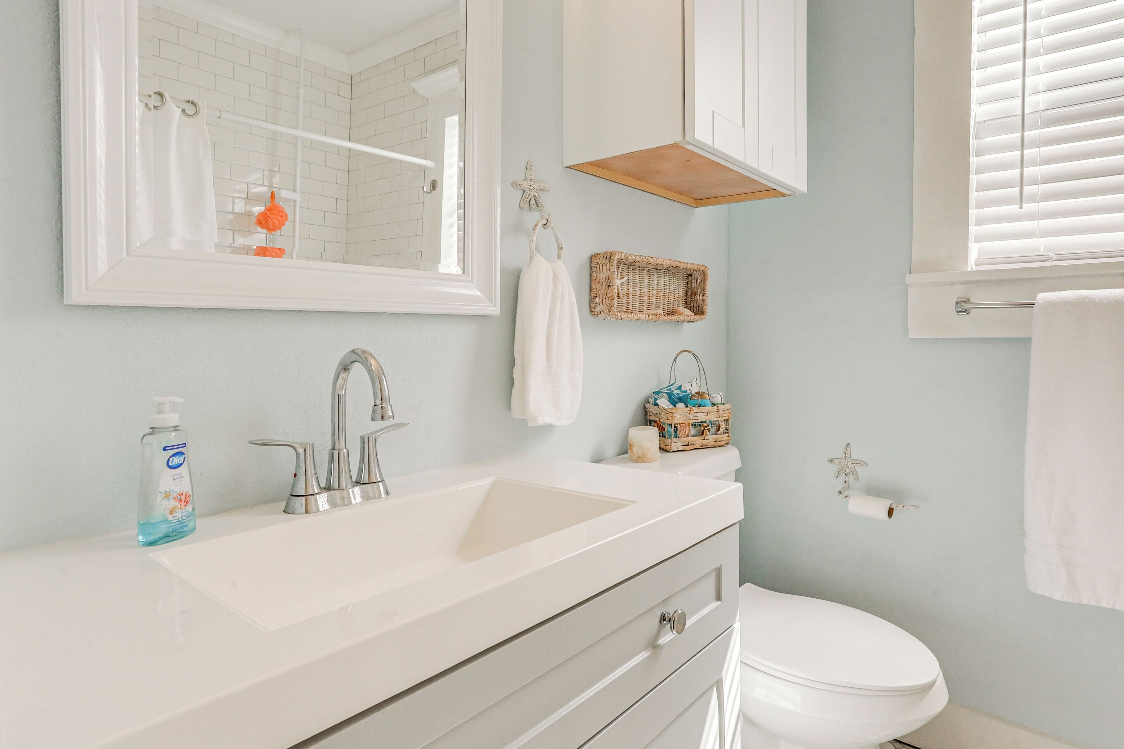 A bathroom with a white sink, a mirror, a toilet, and a window with blinds.