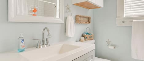 A bathroom with a white sink, a mirror, a toilet, and a window with blinds.
