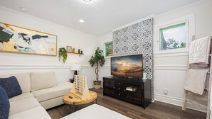 Una sala de estar con sofá, televisión, un muro decorativo y una ventana con vistas.