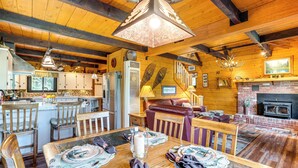 A rustic cabin interior with a wooden dining table set for four, a fireplace, and a kitchen area with wooden cabinets and a hanging light fixture. - 24str-00023 Fairplay Cabin w/ Hot Tub on 4 Acres! (Fairplay)