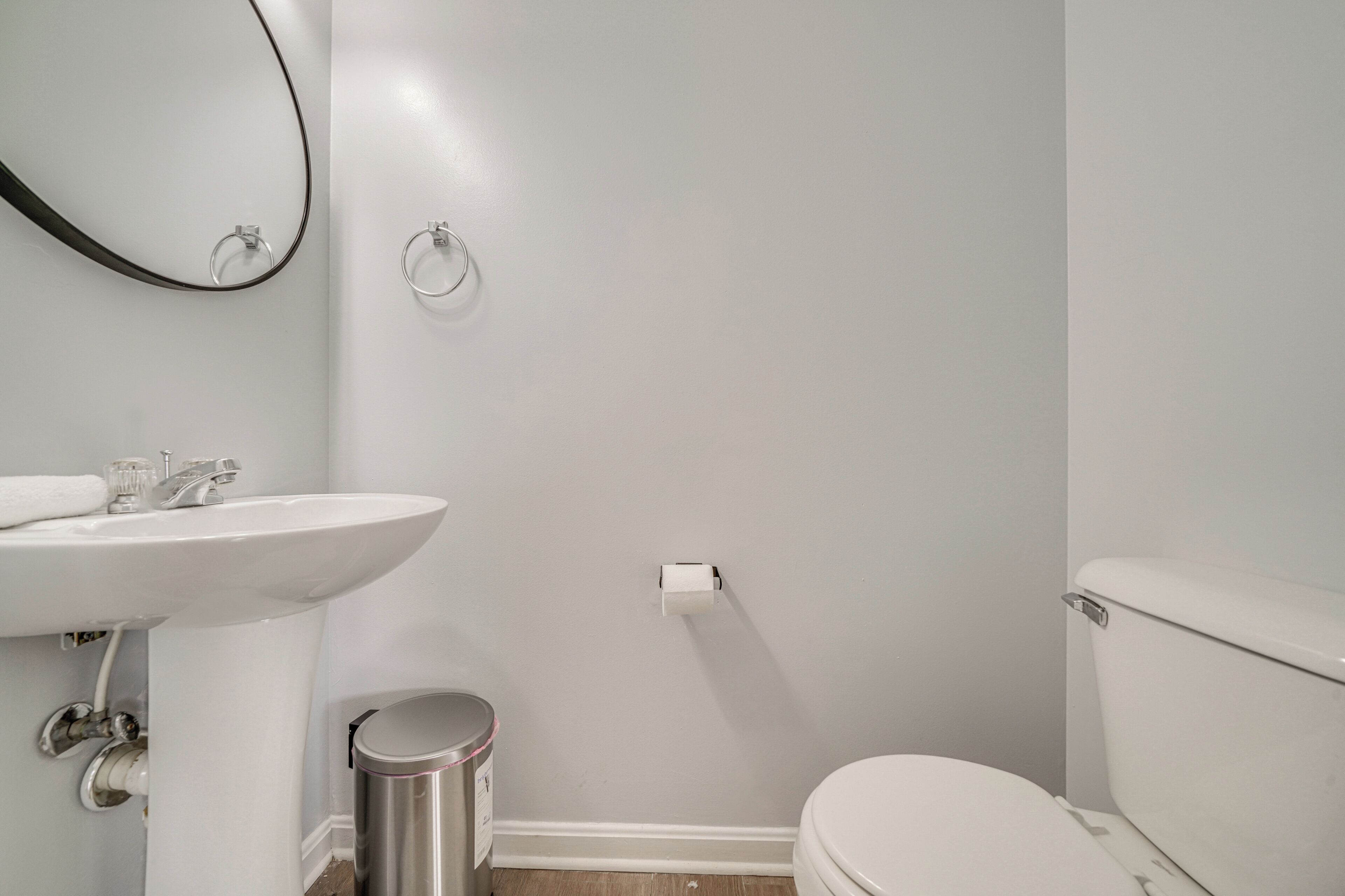 A bathroom with a white sink, mirror, toilet, and trash can.